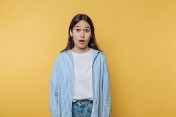 Surprised young woman expresses her astonishment in front of a bright yellow background during a...