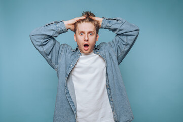 Surprised young man expresses shock with hands on head against a solid blue backdrop