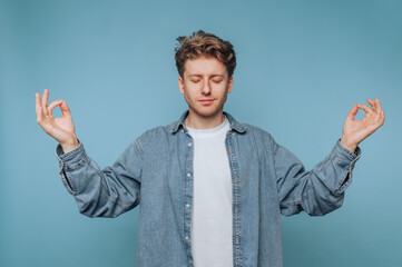 Young man practicing mindfulness meditation against a calming blue backdrop in a peaceful indoor...