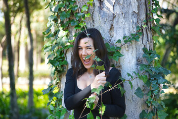 Young, pretty, brunette woman, black T-shirt and jeans, leaning on the trunk of a tree, playing...