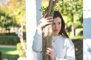 Portrait of a young, beautiful, dark-haired woman in a white dress, with a sweet and dreamy look, clinging to the trunk of a vine. Concept beauty, fashion, trend, femininity, nature, plants, trees.