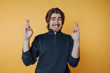 Young man expresses hope and excitement while crossing fingers against a vibrant yellow background...