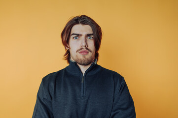 Young man with surprised expression stands against vibrant yellow background showcasing casual style and unexpected emotions