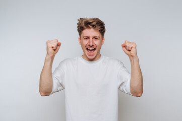 Young man celebrates victory with raised fists, expressing joy and excitement in a bright, neutral...