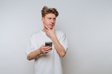 Young man contemplating while holding smartphone in a minimalistic studio environment