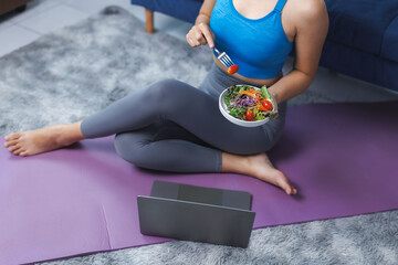 Sporty woman eating salad and watching online training on laptop at home