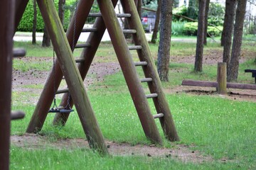Empty wooden playground structure with ladder and swing in a green park. Peaceful outdoor scene...