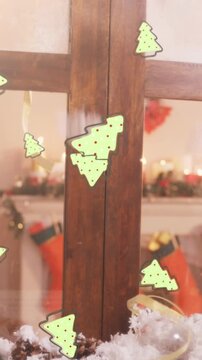 Digital animation of multiple christmas tree icons falling against wooden window frame
