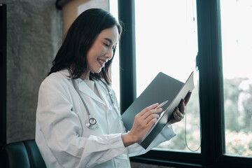 A female doctor in a white coat reviews patient records in a bright, modern medical office.