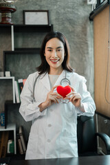 Female doctor in white coat holding a red heart, symbolizing health and care, in a modern medical...