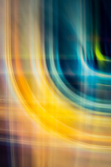 A digital abstract art piece featuring vibrant, overlapping yellow and orange light trails forming fluid, curving lines against a dark, blurred background.