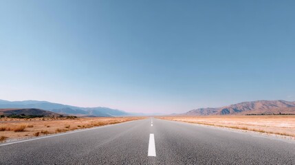 Expansive Open Road Through Desert Landscape Under Clear Blue Sky with Mountains in Background