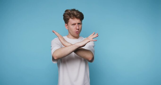young man showing a strong 'no' gesture with his hands, conveying refusal or disagreement on blue background