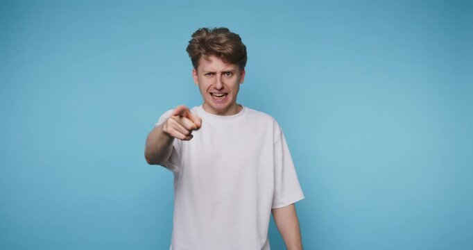 angry young man pointing his finger with a stern expression, manifesting frustration or authority on blue background