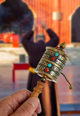 Buddhist Scripture Wheel, hand held spinning Prayer Wheel in front of blurred Buddhist monk praying...