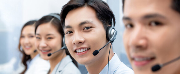 Asian man telemarketer wearing headset with microphone working with colleagues in call center office