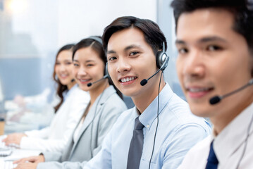 Asian male telemarketer wearing headset with microphone working with colleagues in call center...