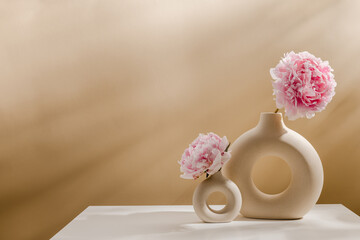 Set of stylish ceramic vase with peony flowers and sunlight shadows on the table, copy space. Aesthetic composition for poster, home interior or design.