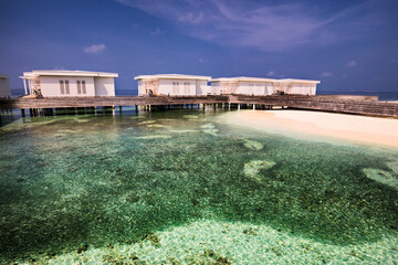 View of overwater bungalows stand elegantly above the crystal-clear turquoise waters meeting the pristine white sand, a serene island escape, Amilla Fushi, Baa Atoll, Maldives.
