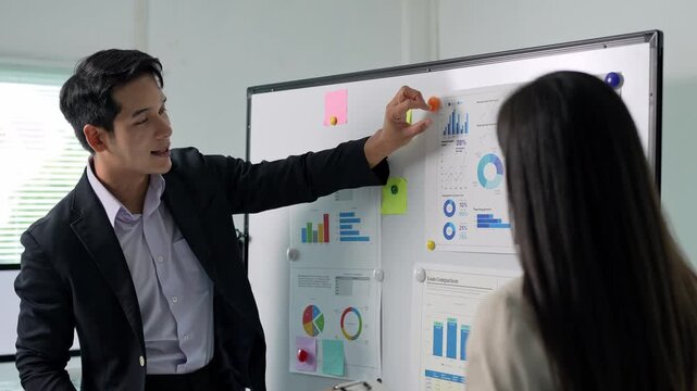 Businessman explaining charts on whiteboard to colleague
