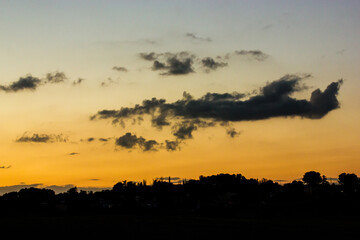 Vibrant sunset with dynamic clouds and a silhouetted landscape. A stunning sunset paints the sky with vibrant hues, silhouetting a distant treeline under a dramatic cloudscape. Yellow sky.