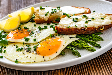 Crispy toasted bread with cheese, green asparagus and fried eggs with runny yolks on wooden table	