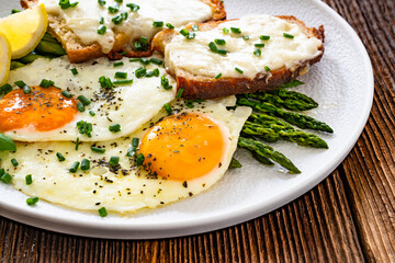 Crispy toasted bread with cheese, green asparagus and fried eggs with runny yolks on wooden table	