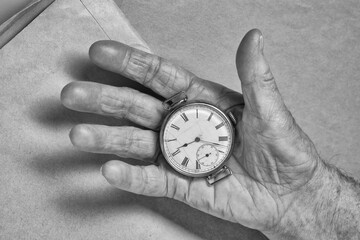 A cracked  antique wristwatch face in an old woman's hand. Top view. Toned image, black and white.