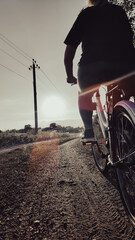 Woman riding cruiser bike riding in remote area on sunset. Back view. Cyclist girl biker enjoys freedom, healthy lifestyle, sport activity. Active summer holidays.