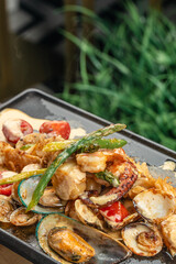 A sizzling seafood medley with shrimp, mussels, clams, and vegetables served hot on a black grill...