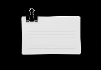 A compact stack of white, lined paper is secured by a black binder clip on a black surface