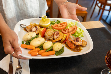 Waitress serving grilled seafood skewer with vegetables and sauce