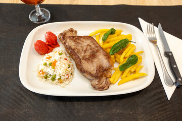 Grilled beef steak served with french fries, rice and padron peppers