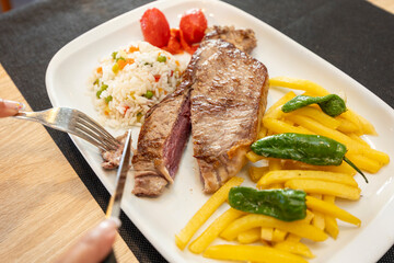 Customer cutting grilled beef steak with knife and fork in restaurant