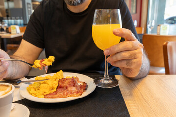 Customer enjoying breakfast with scrambled eggs, bacon, and orange juice in restaurant
