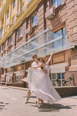 Elegant couple dances gracefully on a sunlit urban street with tall buildings adding to the urban...