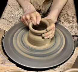 Hobbies and creativity. Closeup of clay product being made on pottery wheel. Hands of young craftsman forming clay pot on pottery wheel.