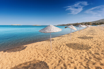 Golden sand beach with straw umbrellas by the calm sea water under a blue sky, creating a relaxing summer vacation atmosphere