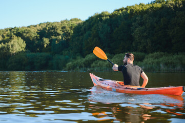Kayaker paddling on a lake next to a forest during a sunny summer day