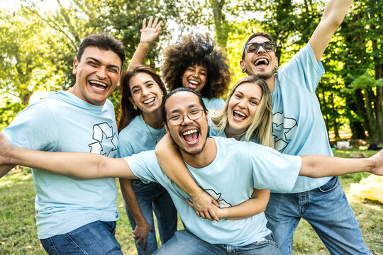Multi ethnic group of volunteers cleaning up a forest together - Happy team of environmental activists smiling at camera outdoors - Environmental protection and non profits organization concept