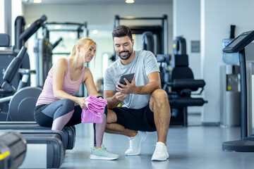 Mid adult woman and personal fitness trainer having conversation during workout break at gym.