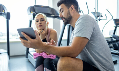 Mid adult woman and personal fitness trainer having conversation during workout break at gym.