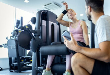 Mid adult woman and personal fitness trainer having conversation during workout at gym.