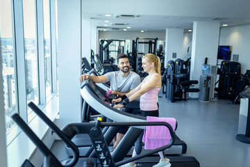 Mid adult woman and personal fitness trainer preparing for workout on treadmill at gym.