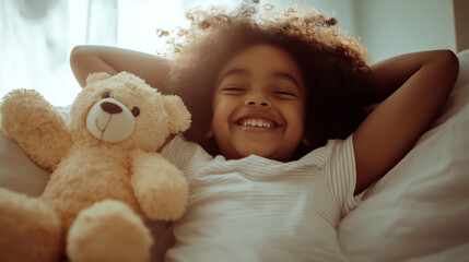 Joyful Black child stretching in bed with a teddy bear on a sunny morning