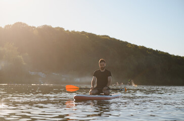 Man kneeling on sup board paddling at sunset on a lake