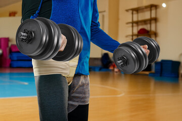 Male athlete after medical operation wearing supportive hernia bandage while lifting dumbbells at...