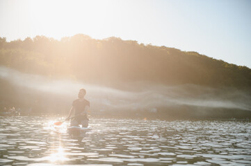 Man enjoying sapsurfing on calm lake at sunrise