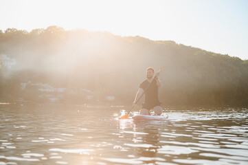 Man kneeling on sup board paddling on lake at sunset