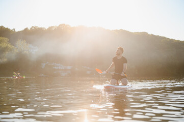 Sportsman kneeling on sup board paddling on lake at sunset
